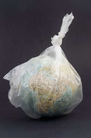 Ecology environmental protection concept. Glass ball in a plastic bag on a black background. Save the planetの写真素材