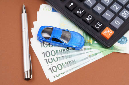 Toy car, calculator and pen on a brown background. Car rental, purchase or insurance. Business conceptの写真素材