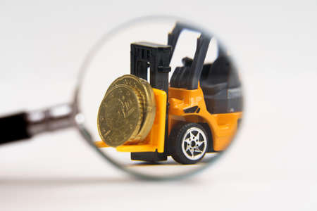 Business and economy concept. A toy loader transports coins. Look through a magnifying glass. Isolated on white background.の写真素材