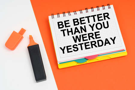 business and finance concept. On a white-orange surface lies a marker and a notepad with the inscription - BE BETTER THAN YOU WERE YESTERDAYの写真素材