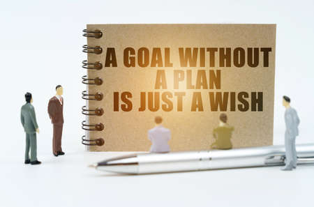 finance and business concept. On a white background there are figures of businessmen, there is a pen on which the figures of businessmen sit and there is a notepad with the inscription - A Goal Without a Plan Is Just a Wishの写真素材