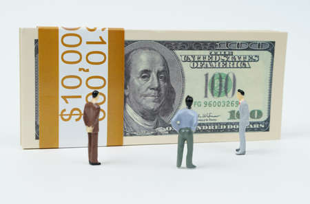 business concept. On a white surface is a pack of dollars and miniature figurines of people. looking at dollarsの写真素材