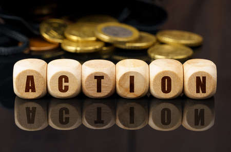 Business and economy concept. On a black reflective surface are coins and wooden cubes with the inscription - ACTIONの写真素材