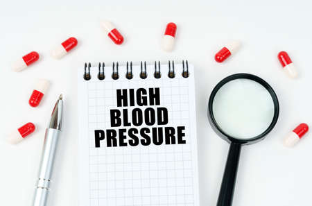 medical concept. On a white surface are tablets, a pen, a magnifying glass and a notepad with the inscription - High blood pressureの写真素材