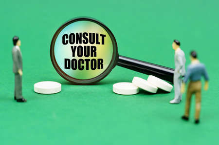 medical concept. On a green surface are pills, miniature figures of people and a magnifying glass with the inscription - Consult your doctorの写真素材