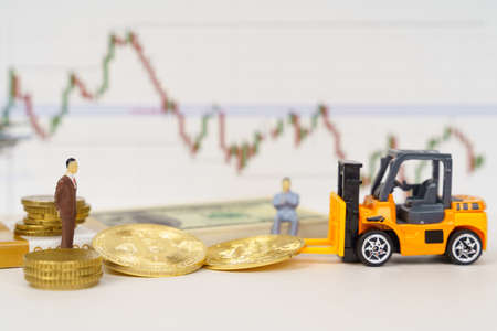 Cryptocurrency and business concept. On a white surface are dollars, bitcoins, a loader, figures of people. In the background is a chart of currency quotes.の写真素材