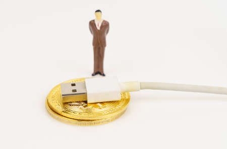 Cryptocurrency and business concept. On a white surface are a bitcoin cord with USB and a miniature human figure.の写真素材