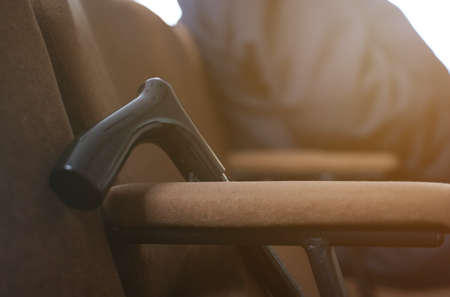 medical concept. There is a wooden cane next to the chair. In the background, a disabled person sits...