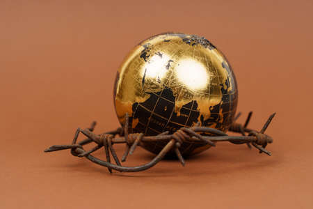 The concept of symbolism. On a brown surface is a globe, which is surrounded by barbed wire.の写真素材