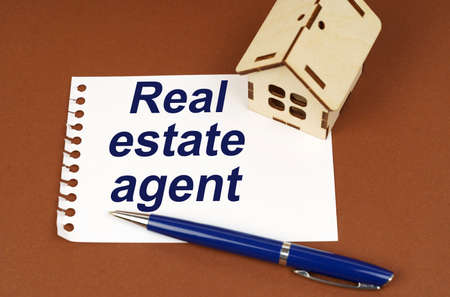 business concept. On a brown surface is a house, a pen and a notepad with the inscription - Real Estate Agentの写真素材