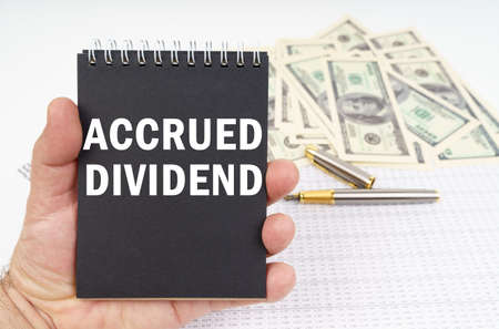 business concept. In the man's hand is a notepad with the inscription - ACCRUED DIVIDEND, in the background a pen and dollars. Pen and dollars blurred.の写真素材