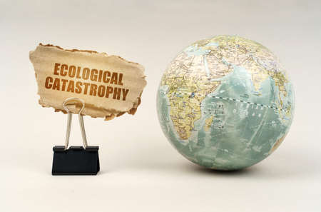 ecological concept. Near the globe there is a clip with a cardboard plate on which it is written - Ecological catastrophyの写真素材