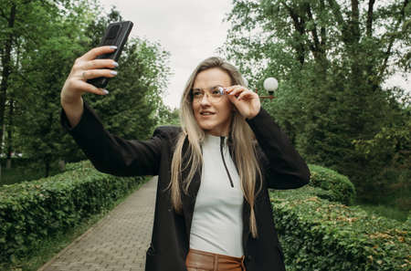 Happy flirting young girl takes a photo of herself on a smartphone in the park. people and technology concept.の写真素材