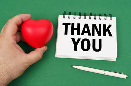 On the green surface are a pen, a notepad with the inscription - THANK YOU. A man has a heart in his hands.の写真素材