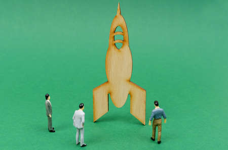 Figures of businessmen stand around a wooden rocket on a green background. innovation concept.
