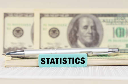 business concept. On the dollars are a pen and a sign with the inscription - STATISTICS. In the background in a blurred background are dollarsの写真素材