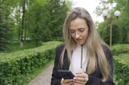 A woman reads and types messages on a smartphone. A woman walks in the park and looks at her mobile...