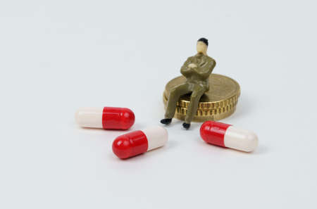 A miniature figurine of a man sits on coins next to him medical capsules. treatment costsの写真素材