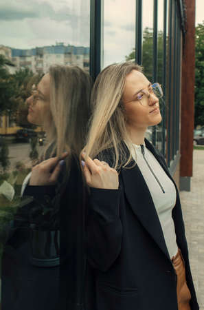 A beautiful woman stands leaning against the window of a building, touches her hair with her hands, looks into the distance. Portrait of a beautiful woman.の写真素材