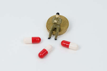 A miniature figurine of a man sits on coins next to him medical capsules. treatment costs