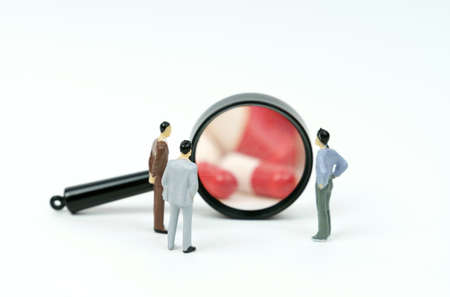 Three miniature figures of people look through a magnifying glass at medical capsules. The concept of medical access.の写真素材