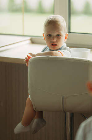 Portrait of a disgruntled little boy sitting on a chair by the window. portrait of a childの写真素材