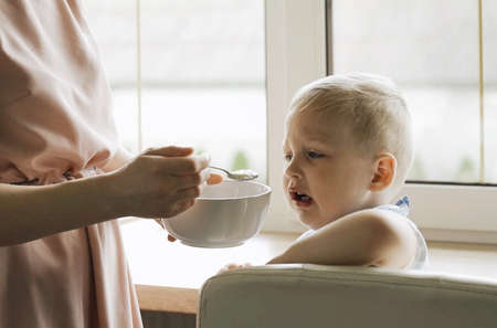 Mom feeds the boy porridge with a spoon from a plate. close-upの写真素材