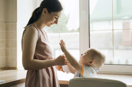 Mom feeds the boy porridge with a spoon from a plate. The boy does not want to eat. Asking for handsの写真素材