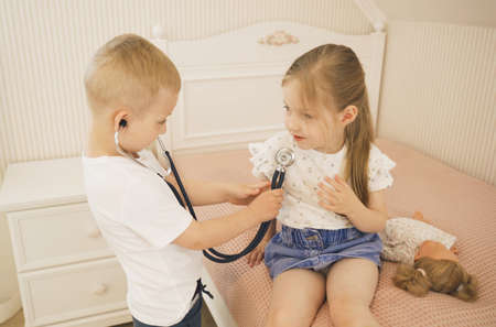 A boy listens to a girl with a stethoscope. They play doctor. children's games.の写真素材