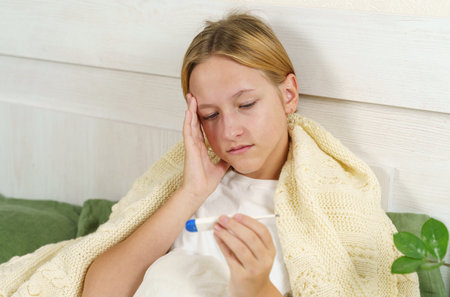 The sick girl looks at the thermometer and holds her head with her hand. The concept of health and...