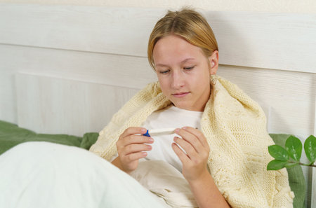 A sick girl sleeps in bed covered with a blanket, a thermometer lies nearby. medicine and health...