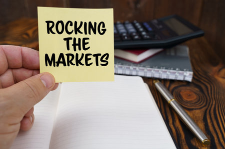 business concept. In the hands of a man is a sticker with the inscription - Rocking the Markets. In the background in a blurred background are office items.の写真素材