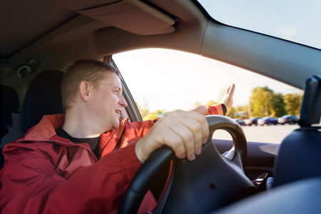 A happy man looks out of the car window and greets someone with his hand.の写真素材