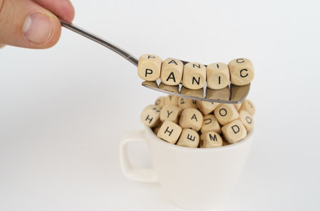 business concept. Cubes with the image of letters are poured into the cup, above the cup there is a spoon with cubes with the inscription - Panicの写真素材