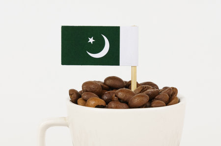 The flag of Pakistan sticks out of a cup of roasted coffee beans. Concept of consumption and...