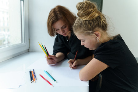 A happy family. Mom and daughter are painting together, sitting by the window.の写真素材