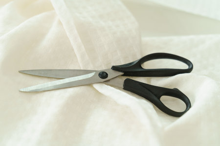 Cutting textile or fine cloth with a tailor scissors on wooden table. Sewing toolsの写真素材