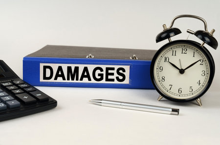 business concept. On a white surface, an alarm clock calculator and a folder with the inscription - damagesの写真素材