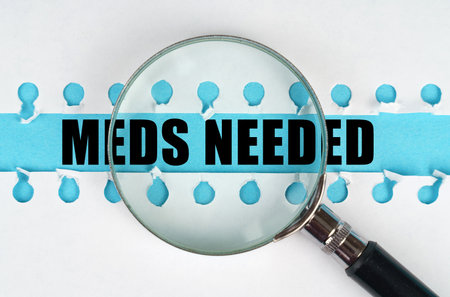 Between two sheets from a notebook on a blue stripe with the inscription - Meds Needed, there is a magnifying glass. medical concept.の写真素材