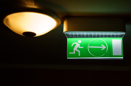 A green warning light board depicting a running man with an arrow. There is a lamp next to the sign....
