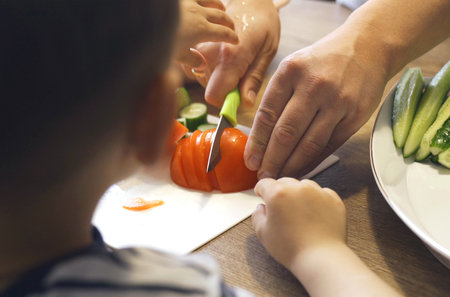 Dad cuts a tomato with a knife, the son wants to help him. close-up.