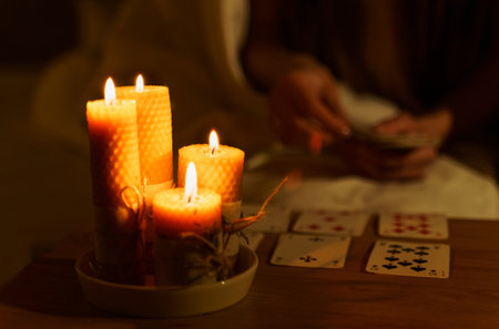 A woman fortune-telling with cards in a dark room by the light of burning candles. Image of candles...