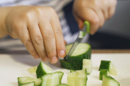 A little boy cuts a cucumber with a knife. close-up.の写真素材