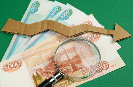 On a green surface lie Russian rubles, a magnifying glass and a cardboard arrow pointing down. The crisis of the economy, the fall of the ruble.の写真素材