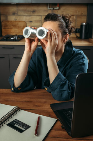 Portrait of a beautiful cheerful female clothing stylist who sits at a table near a laptop and looks through large spools of thread. vertical frame.の写真素材