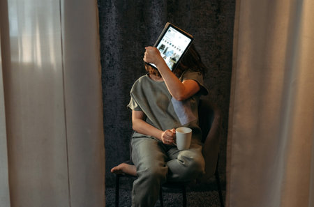 Portrait of a young woman who covers her face with a tablet.