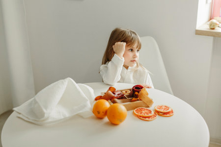 A girl in a white coat sits at a table, looks away, is going to eat marmalade.の写真素材