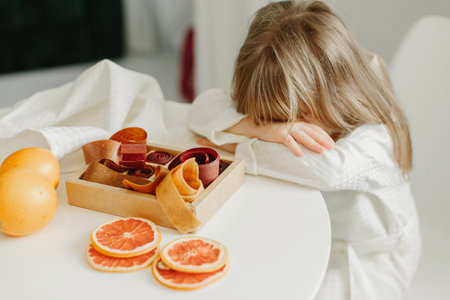 A girl in a white coat fell asleep or is sad sitting at a table on which stands a fruit marshmallow.の写真素材