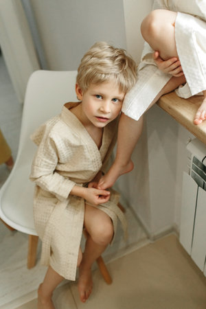 Portrait of a blond boy in a dressing gown, who sits on a chair and leans on his brother's leg.の写真素材
