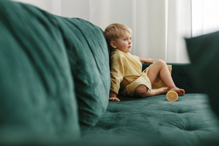 A portrait of a boy in a yellow bathrobe sits on a green sofa, next to it lies half an orange.の写真素材